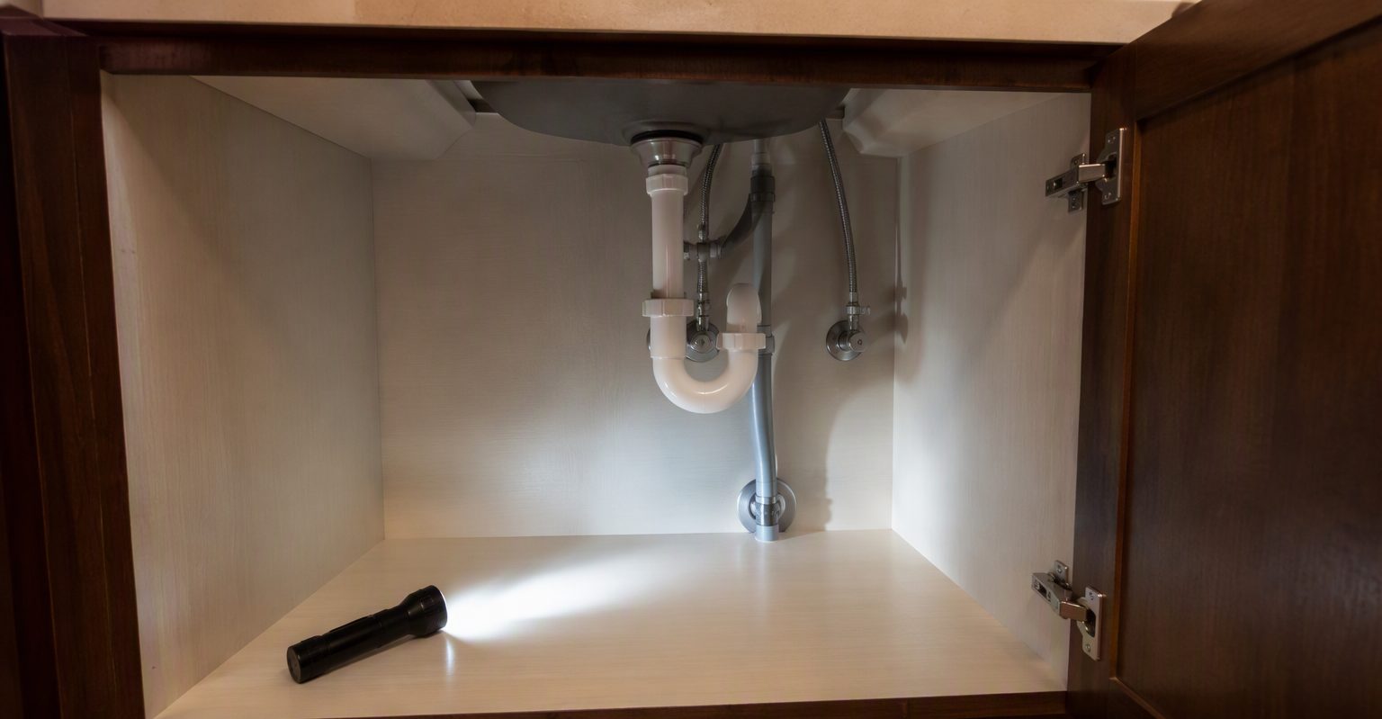 Clean empty under-sink kitchen cabinet with a flashlight beam